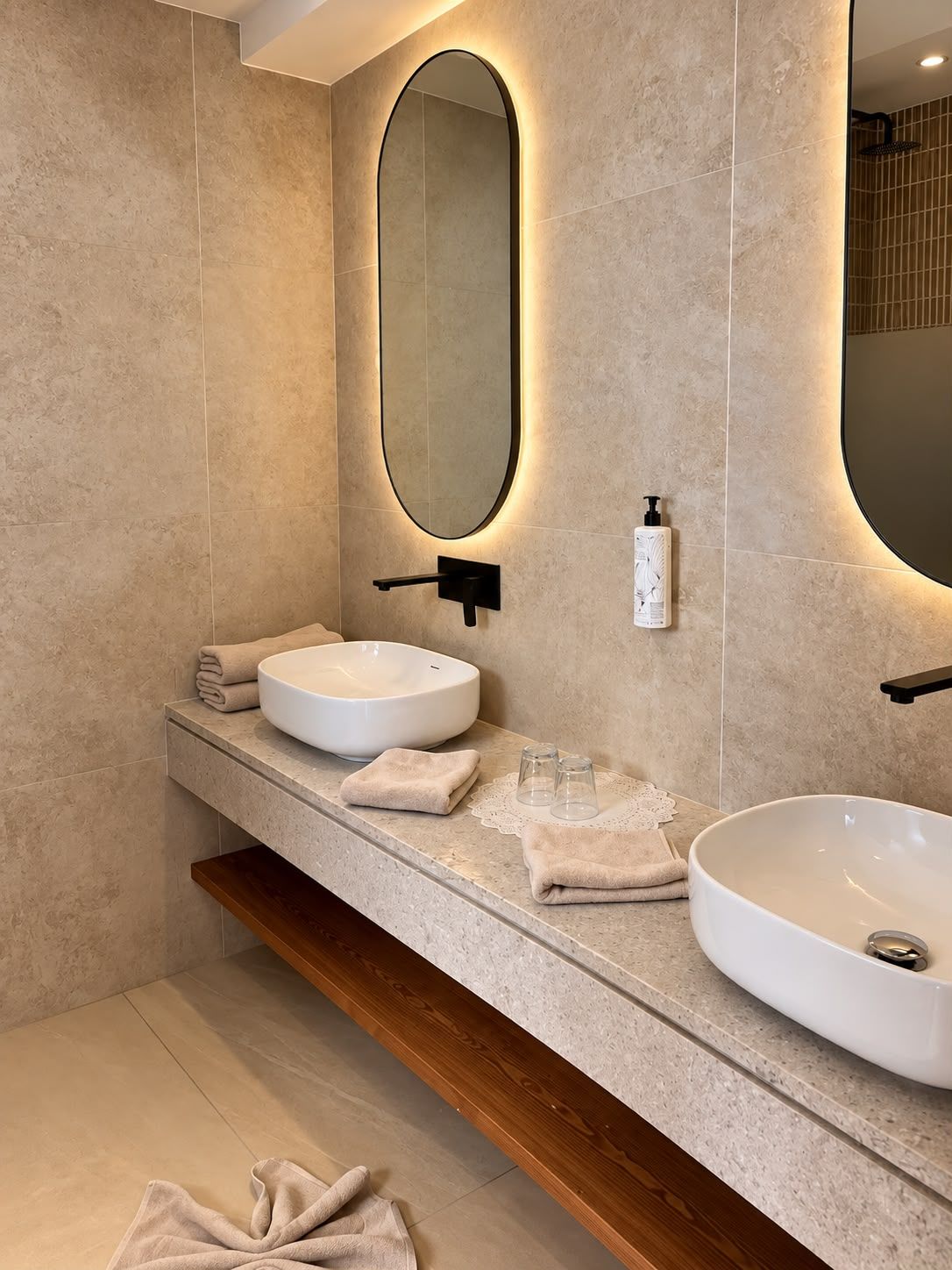 Une salle de bain moderne avec un grand miroir ovale, deux vasques et une étagère en bois.