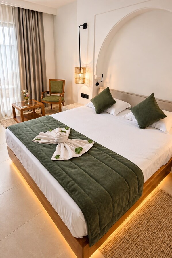 A hotel room with a large bed, a chair, a small table, and a wall-mounted light fixture.