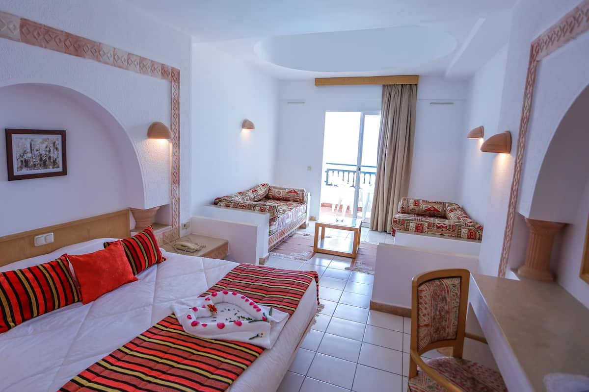 Ein Hotelzimmer mit Bett, Schreibtisch, Stuhl, einem Balkon mit Sitzecke und Blick ins Freie.