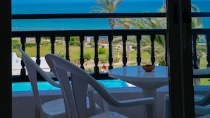 A balcony with white plastic chairs and a small table, overlooking a clear blue sea and palm trees. - Aljazira Beach & Spa  -  Families and Couples Only (Mezraia)