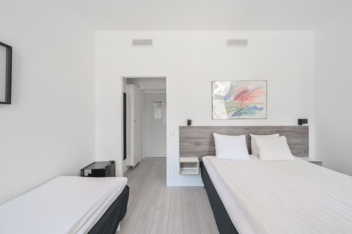 A modern hotel room with two beds, a wooden headboard, a small bedside table, and a colorful abstract painting on the wall.