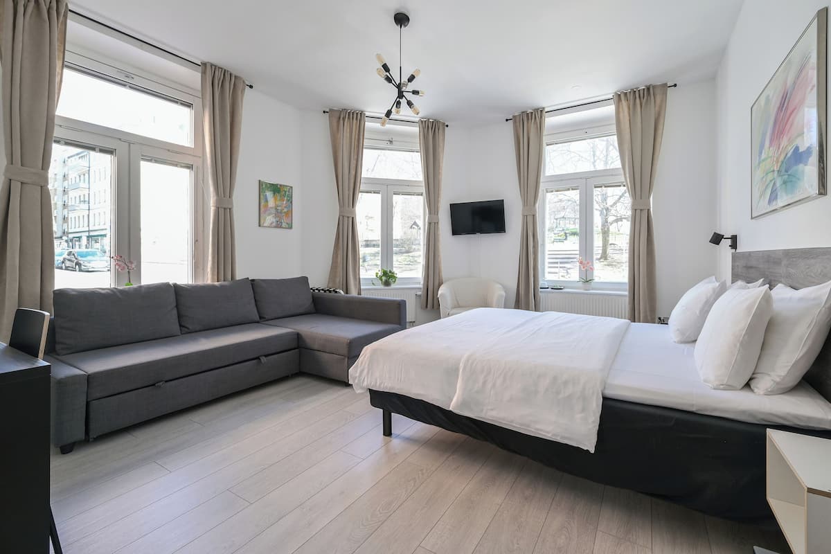 A modern bedroom with a bed, a sofa, a chair, and a TV on the wall.