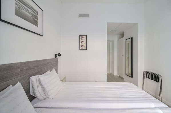 A hotel room with a neatly made bed, a headboard, a framed picture on the wall, a mirror, and a radiator.