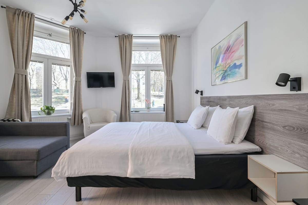 A modern hotel room with a large bed, a sofa, a TV, and a painting on the wall.