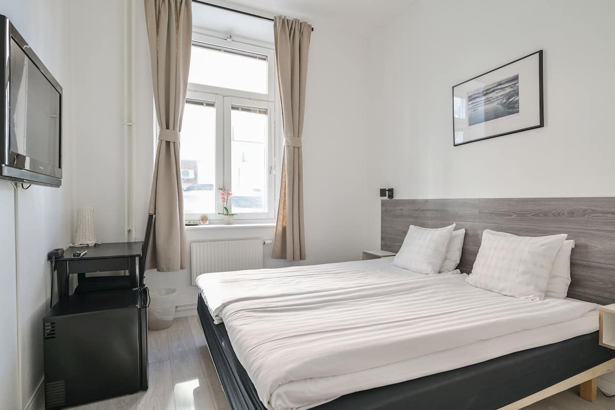 A modern bedroom with a bed, a TV, a small table, and a window with curtains.