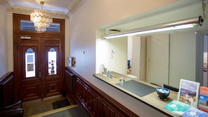A reception area with a wooden reception desk, a large mirror, and a chandelier. - Hotel Bema (Stockholm)