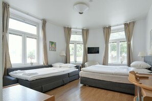 A hotel room with two beds, a desk, a TV, and large windows with curtains. - Hotel Bema (Stockholm)