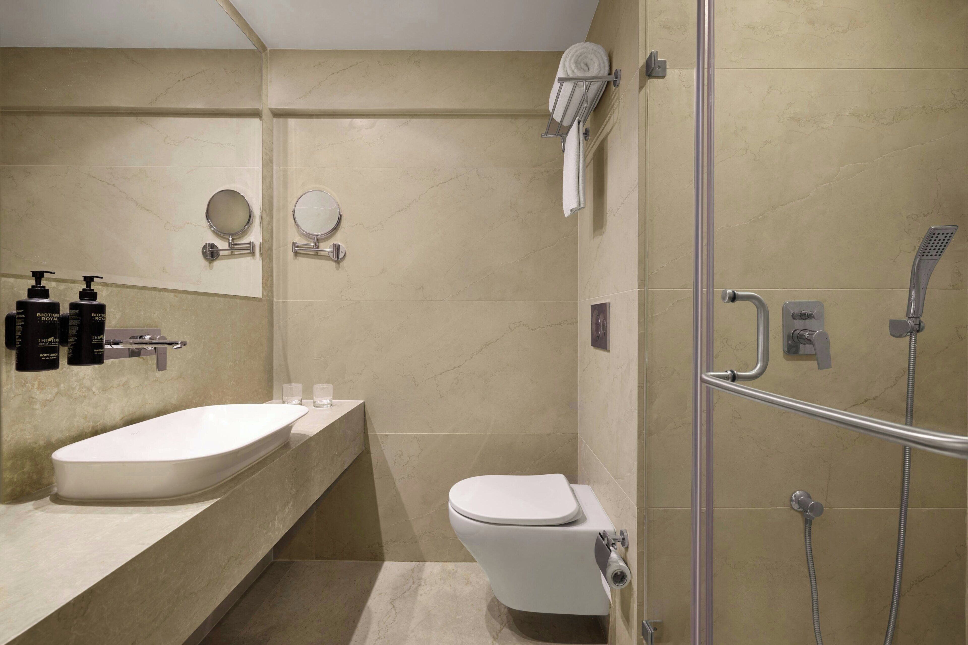 Un baño moderno con una bañera independiente, un inodoro, una ducha con cabezal de ducha manual y dos espejos montados en la pared.