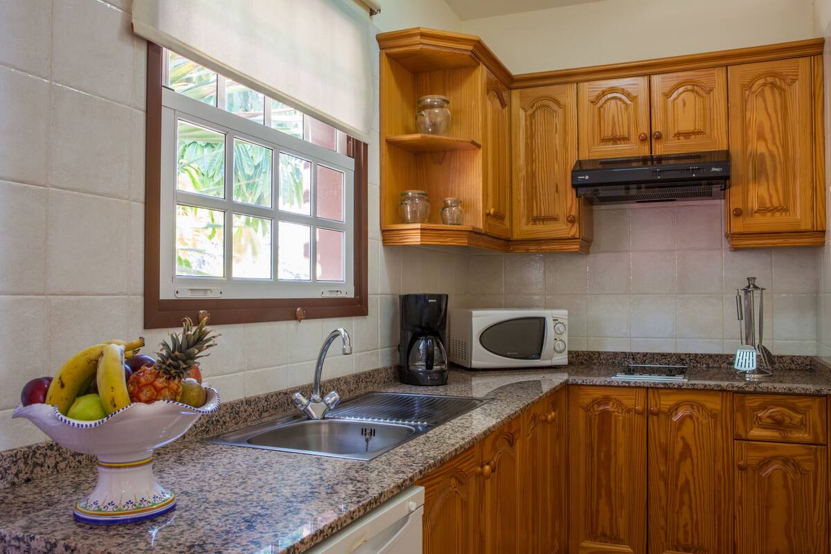 A kitchen with wooden cabinets, a granite countertop, a sink, a microwave, and a fruit bowl.