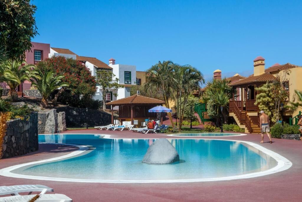 A resort pool area with lounge chairs, a water feature, and palm trees.