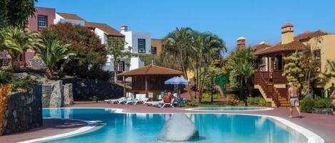A resort pool area with lounge chairs, a water feature, and palm trees.