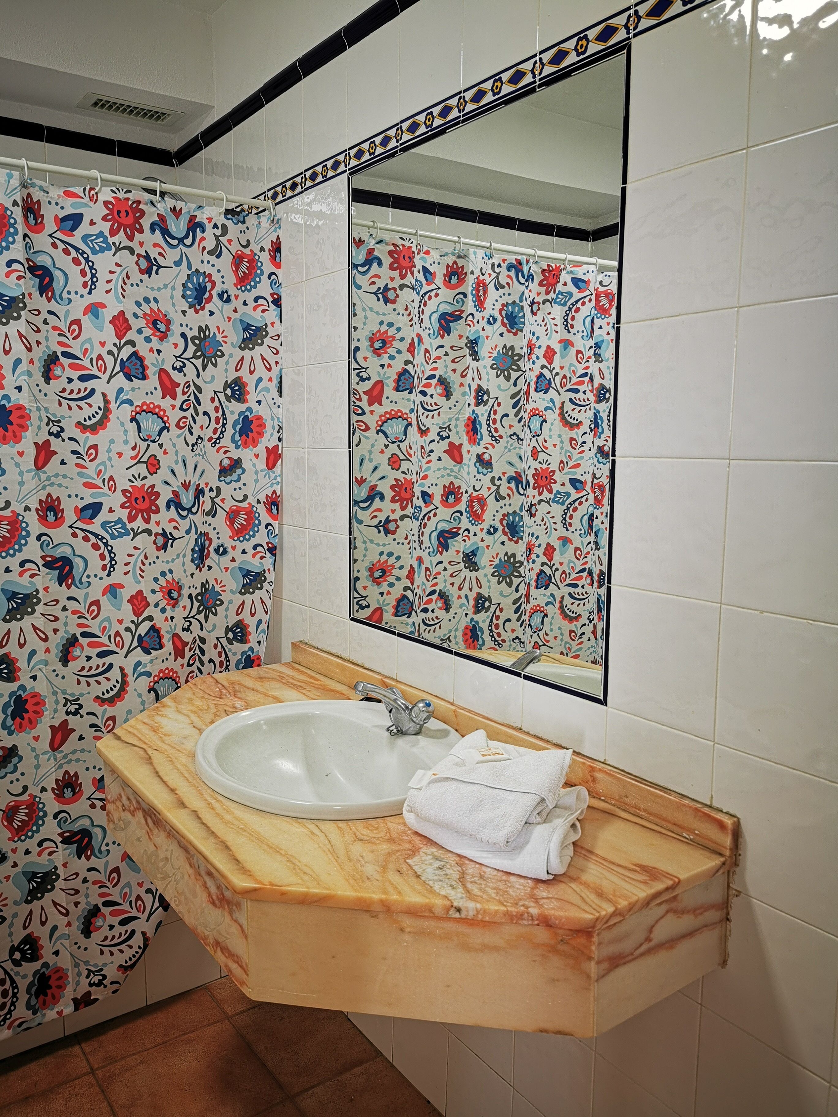 A bathroom with a marble sink, a mirror, and a shower curtain with a floral pattern.