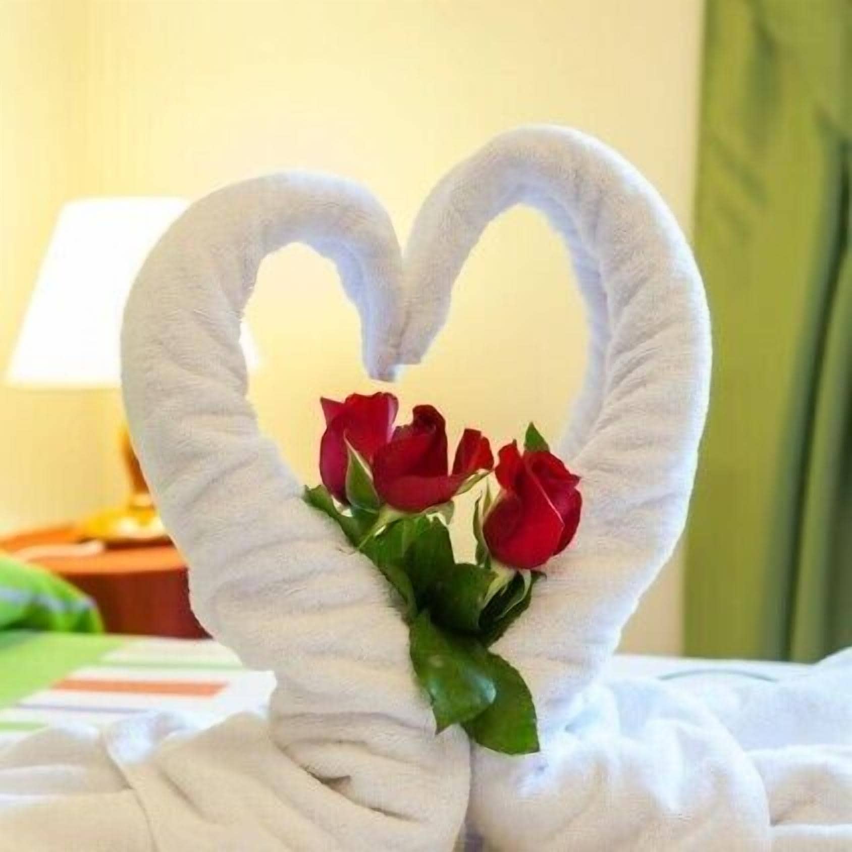 A towel arranged in a heart shape with red roses in the center, placed on a bed.