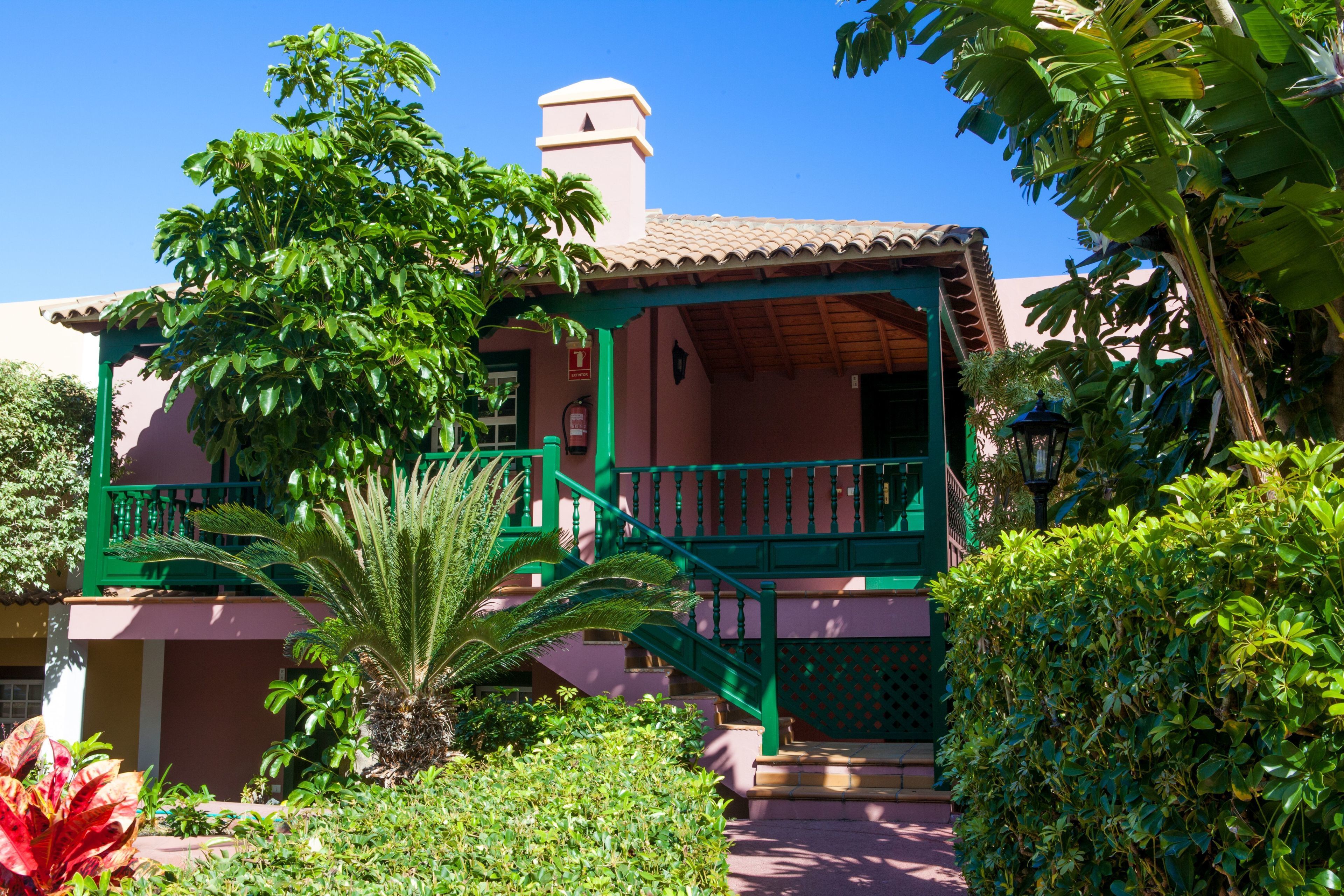 A building with a green balcony, a red door, and a small staircase leading to the entrance.