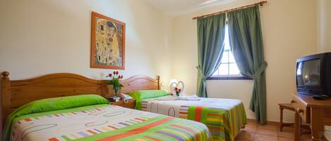 A hotel room with two beds, a television, a painting on the wall, and a window with curtains.
