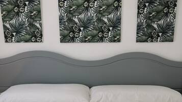 A bedroom with a grey headboard, a bed with white bedding, and three wall-mounted artworks featuring a tropical leaf and flower pattern.