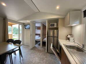 A compact kitchen with a refrigerator, microwave, and coffee maker. There is a dining area with a table and chairs, and a bed is visible in the adjacent room.