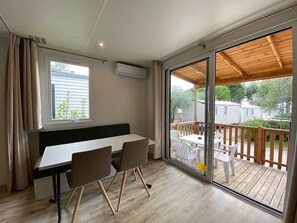 A room with a sliding glass door leading to an outdoor deck, a white table with two chairs, and a bench.