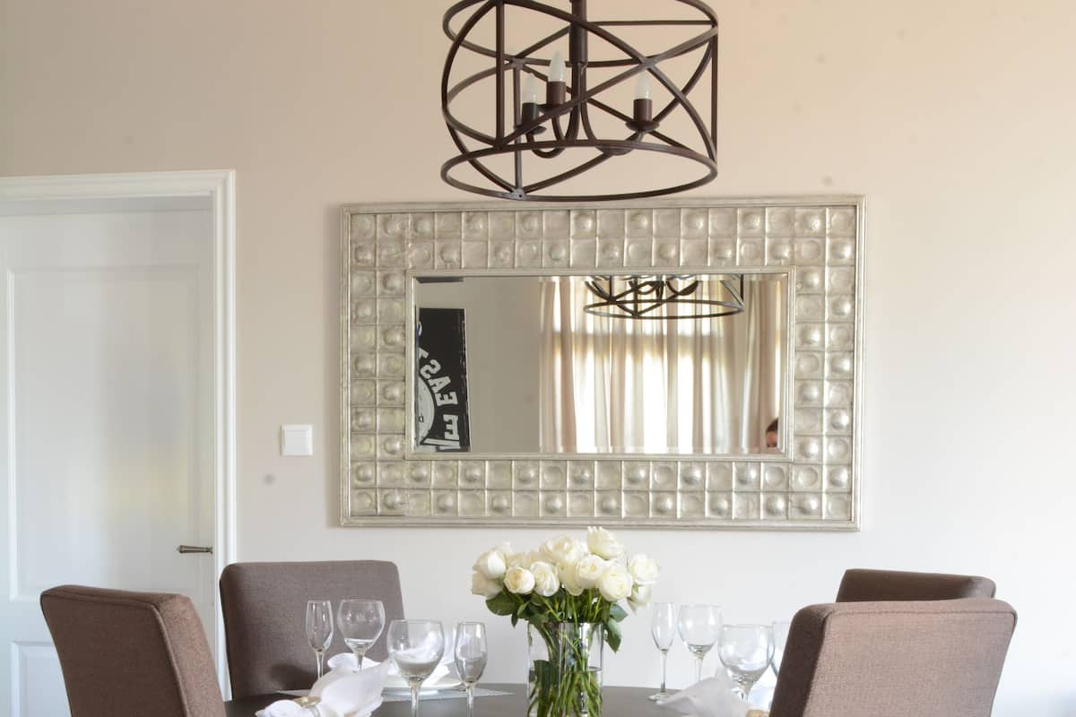 A dining room with a round table, four chairs, a vase of white flowers, and a chandelier.