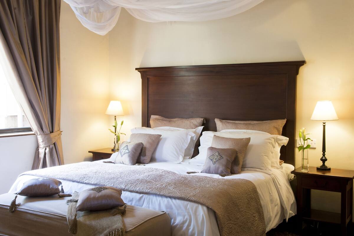 A neatly made bed with multiple pillows and a bedside table with a lamp.