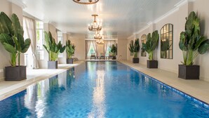 A large indoor swimming pool with a clear blue water surface, surrounded by potted plants and a chandelier. - Palacina The Residence & The Suites (Nairobi)