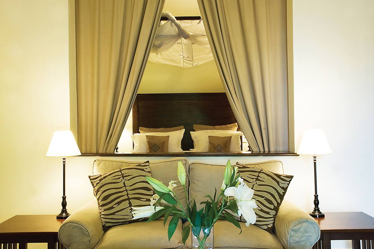 A hotel room with a bed, a sofa, two lamps, and a vase with flowers.