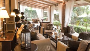 A cozy, well-lit indoor seating area with comfortable sofas and chairs, a table with decorative items, and a view of greenery outside. - Palacina The Residence & The Suites (Nairobi)