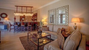 A living room with a sofa, coffee table, and lamps. There is a dining area with chairs and a chandelier. - Palacina The Residence & The Suites (Nairobi)