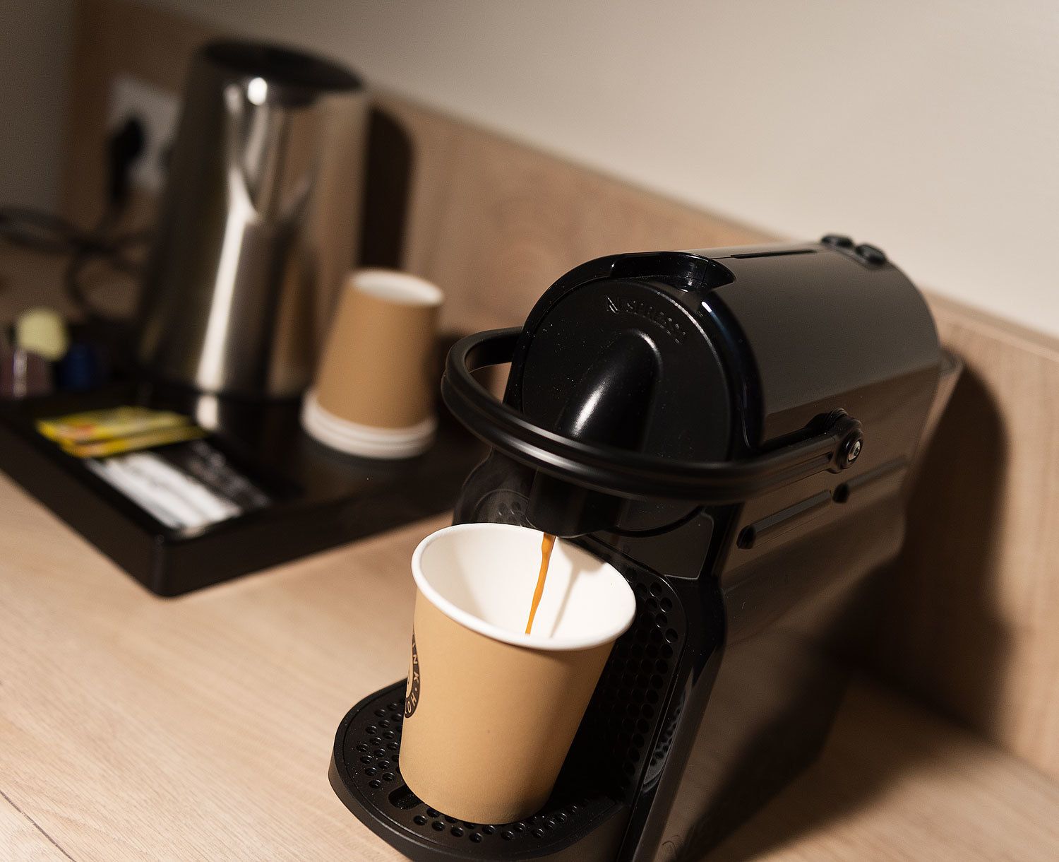 Een koffieapparaat met een kopje op de lekbak, een koffiekan, en een dienblad met een koffiekop en diverse spullen.