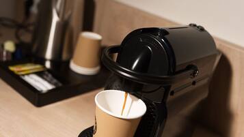 A coffee machine with a cup placed on its drip tray, a coffee pot, and a tray with a coffee cup and some items.