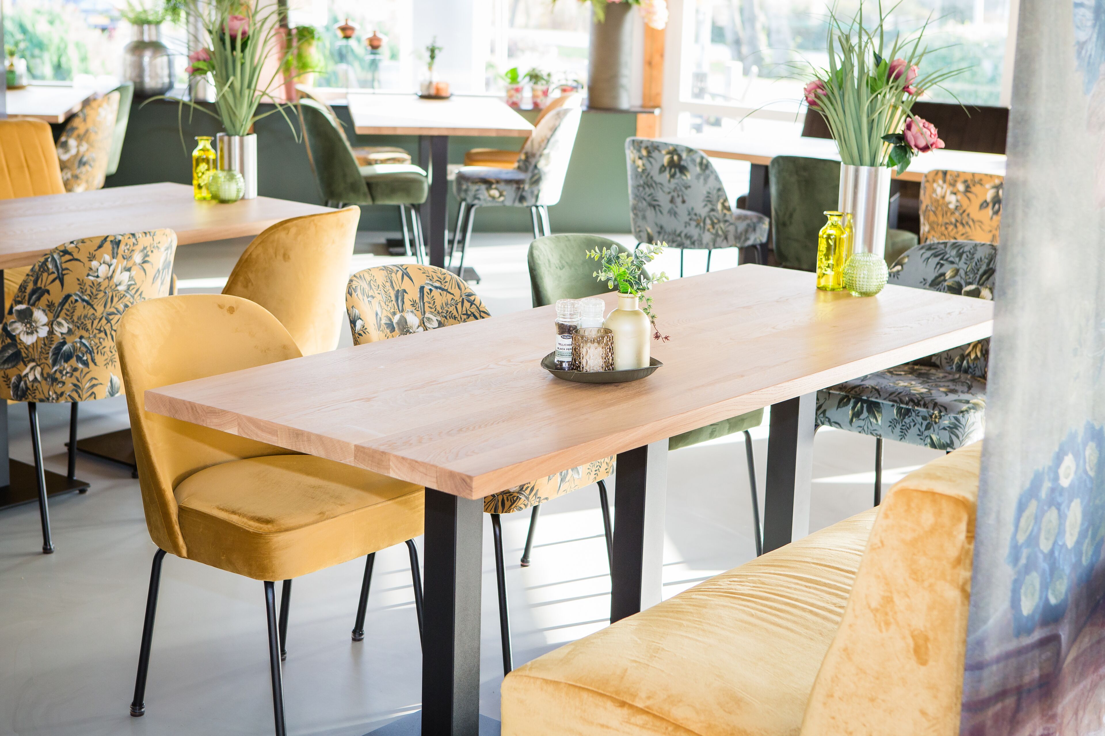 Un coin repas avec une table en bois, des chaises jaunes à motifs et des coussins verts ornés de motifs floraux.