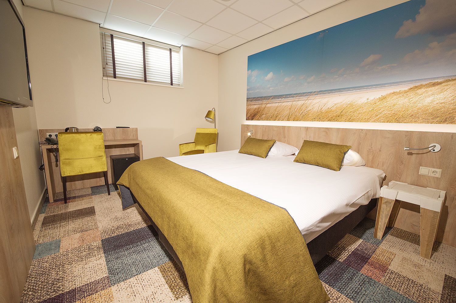 A hotel room with a bed, a desk, a chair, and a large window.