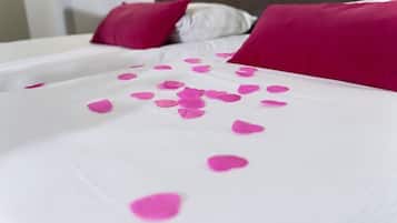 Uma cama com lençóis brancos e pétalas de rosa rosa espalhadas.