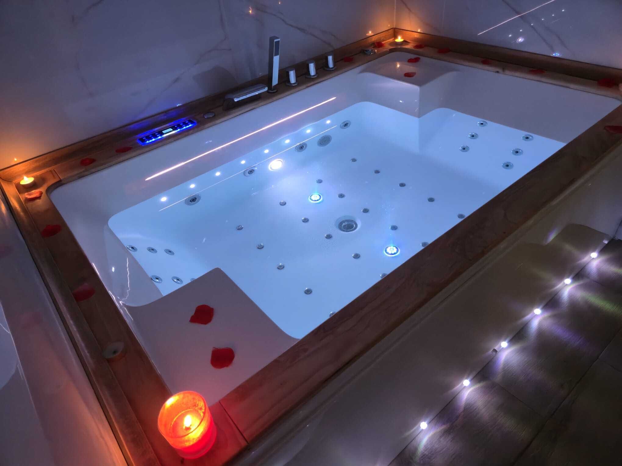 A modern spa tub with LED lighting, a wooden frame, and rose petals.