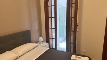 A bedroom with a bed, a nightstand, a lamp, and a view of a balcony through an arched door.