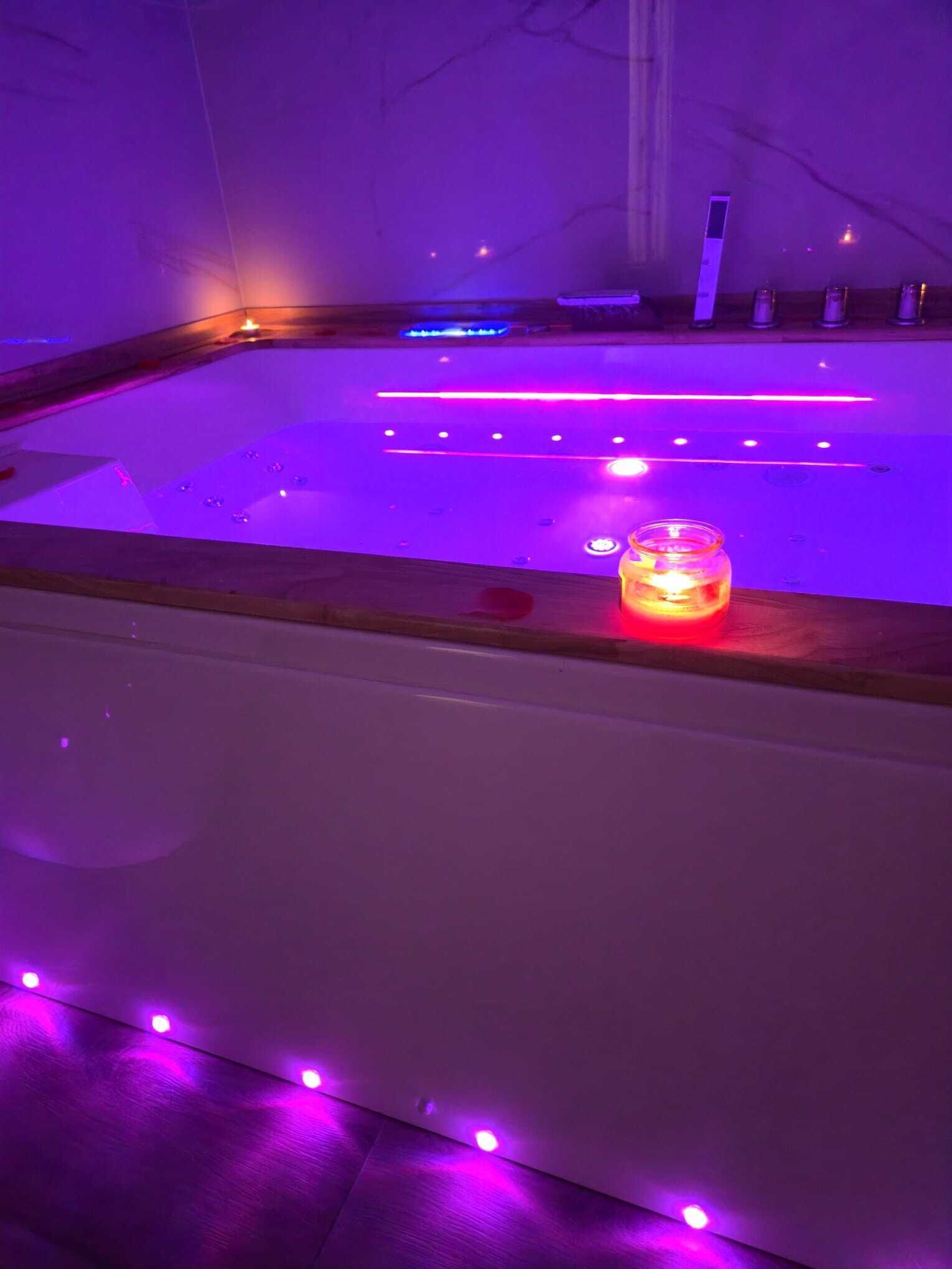 A room with a wooden floor, a glass table with a candle, and purple ambient lighting.
