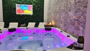 Un bain à remous avec des lumières LED, un panneau lumineux au néon et une bouteille de vin.