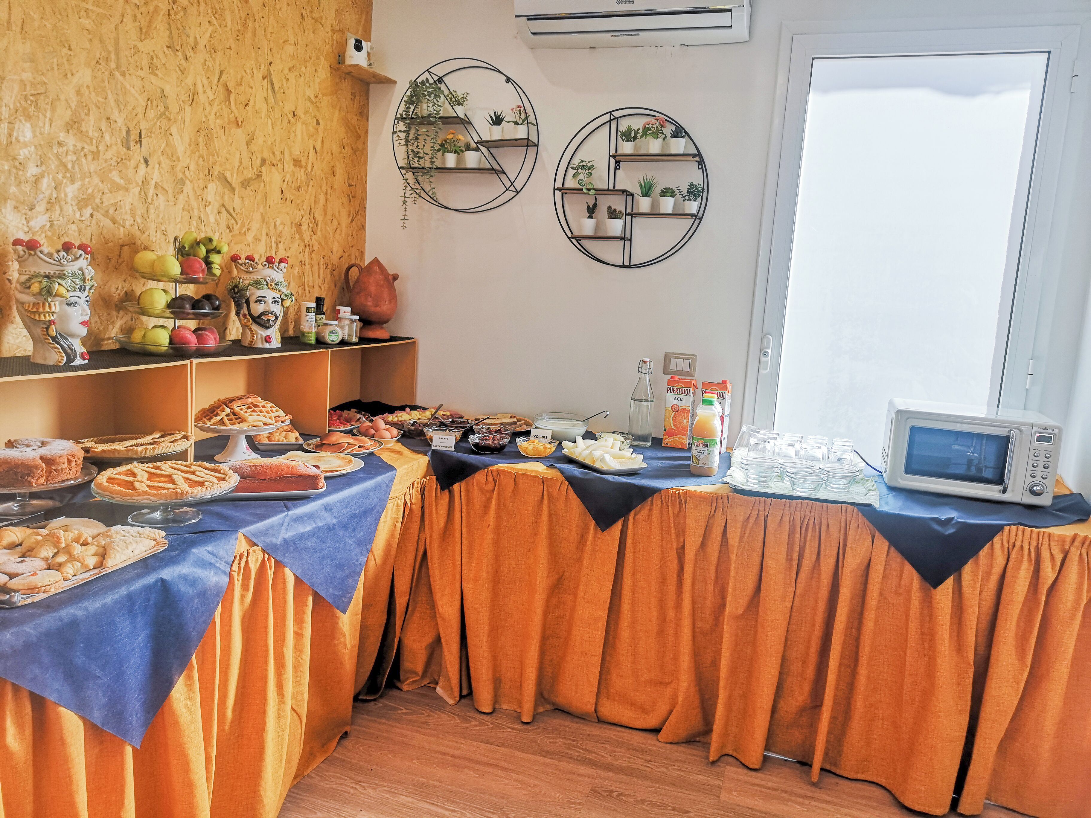 A buffet table with various food items, a microwave, and decorative wall shelves.