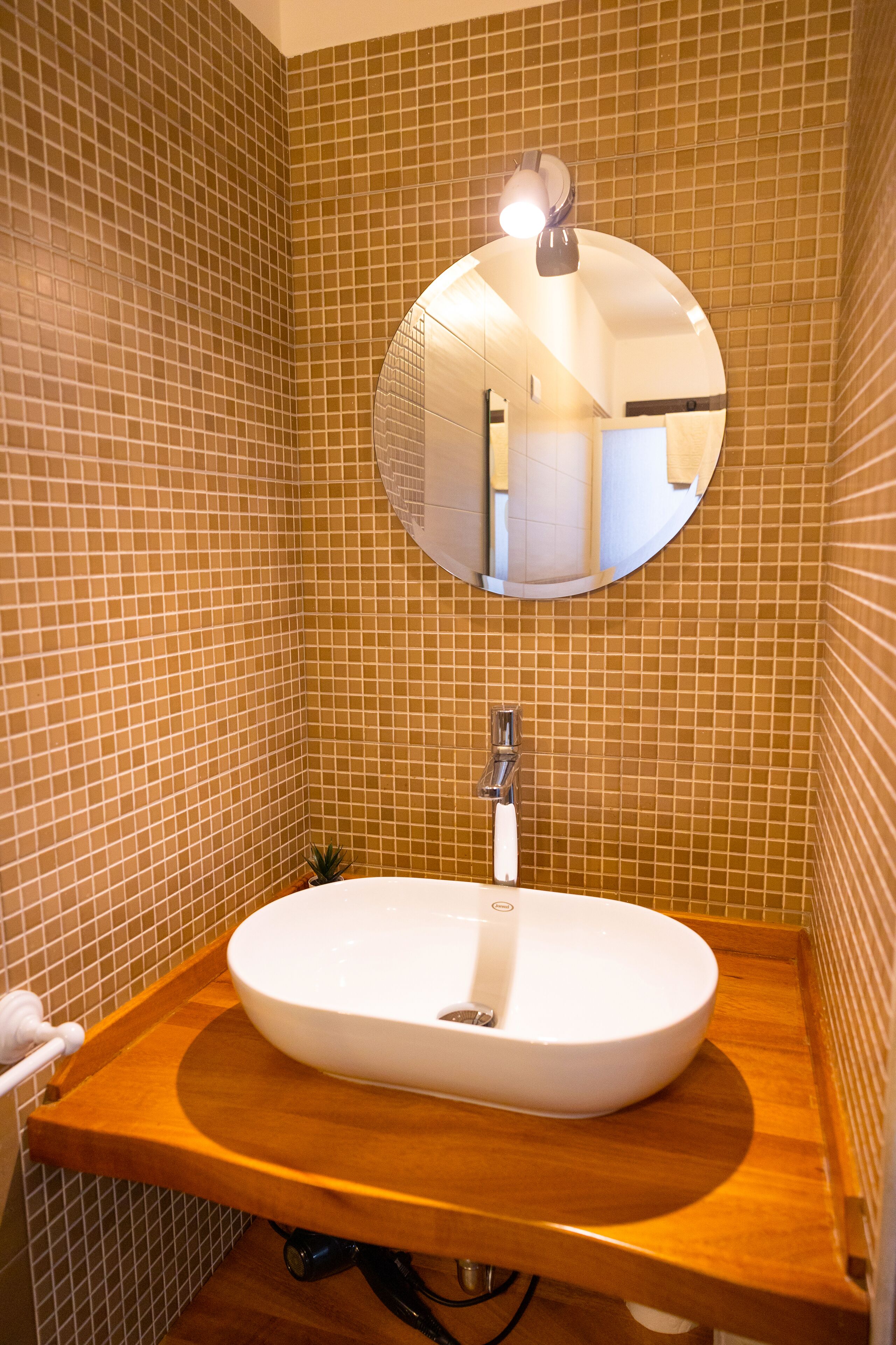 A bathroom with a round mirror, a white sink, and a wooden countertop.