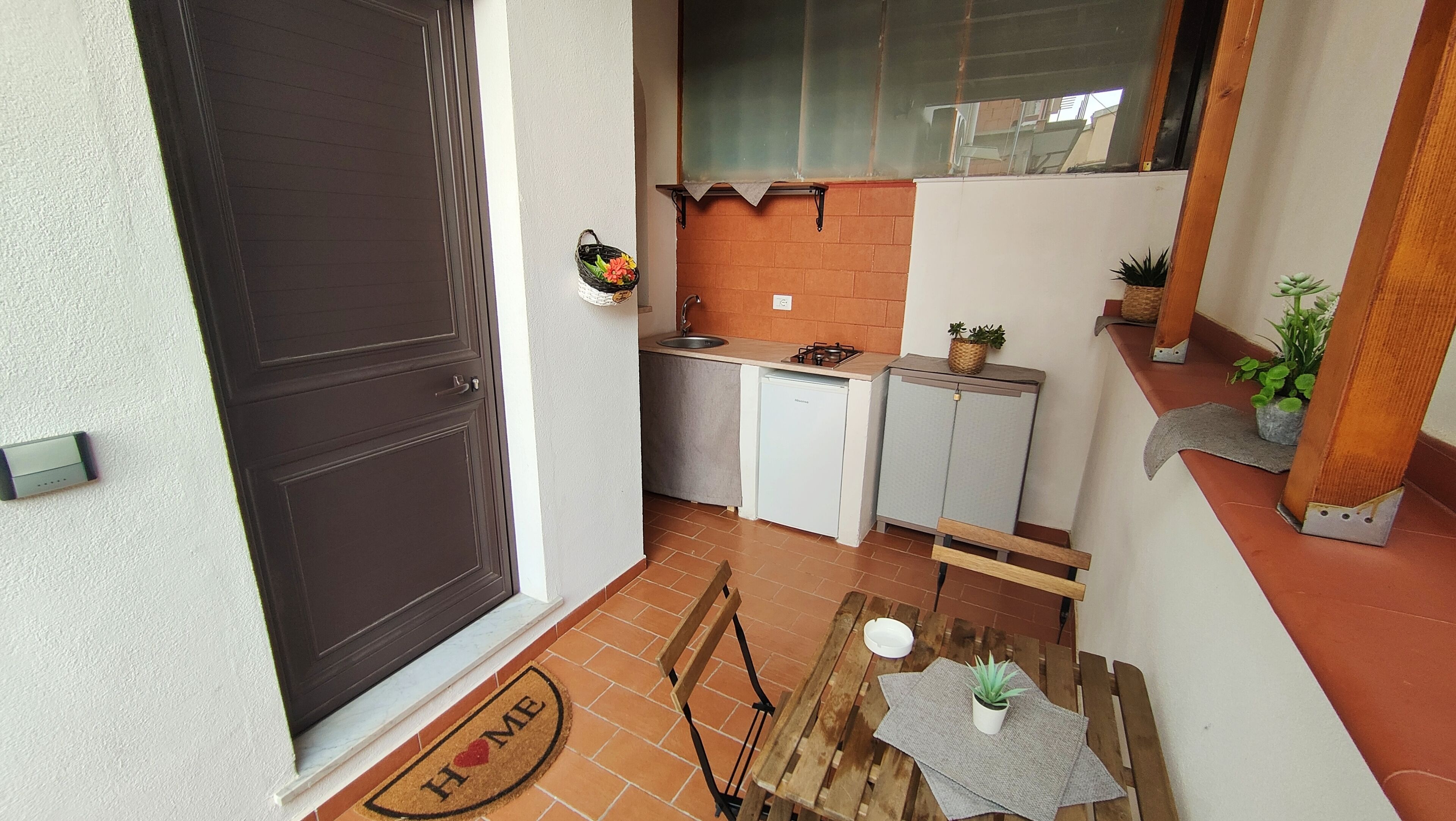 Eine kleine Küche mit Spüle, einem Kühlschrank und einem Herd. Ein hölzerner Bänke und ein kleiner Tisch mit einem Blumentopf.