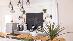 Un café avec un tableau noir servant de panneau, des machines à café, des étagères remplies de plantes et un ordinateur portable posé sur le comptoir.