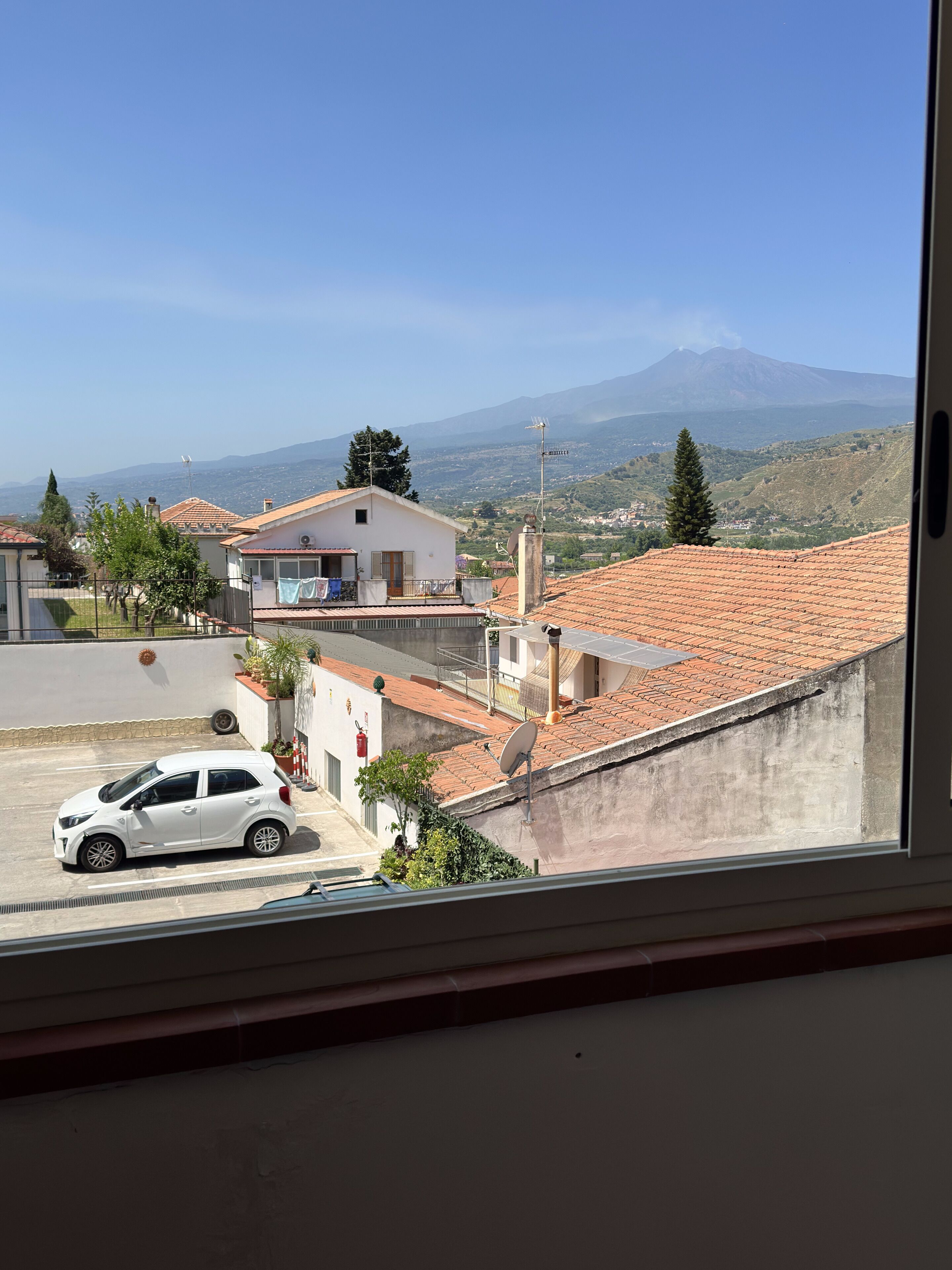 A residential area with a view of a mountain, houses with red-tiled roofs, and a parked car.