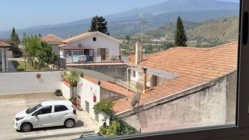 A residential area with a view of a mountain, houses with red-tiled roofs, and a parked car.