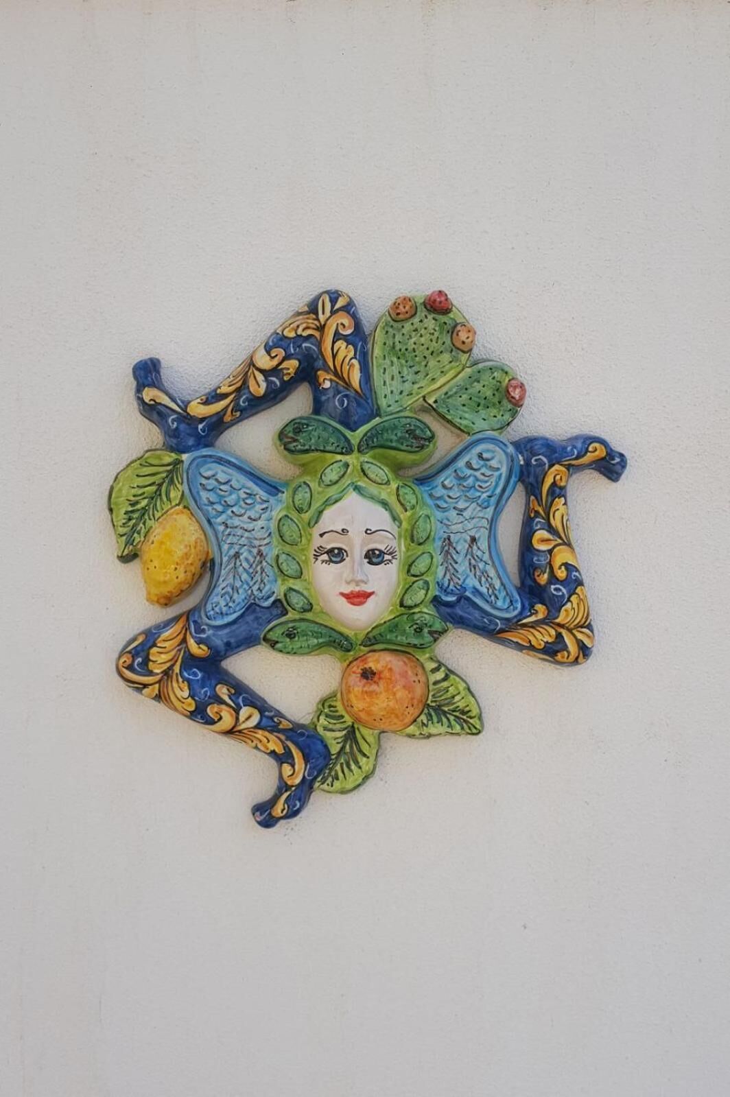 Un élément décoratif mural, composé d’un visage central entouré de motifs floraux et de feuilles.
