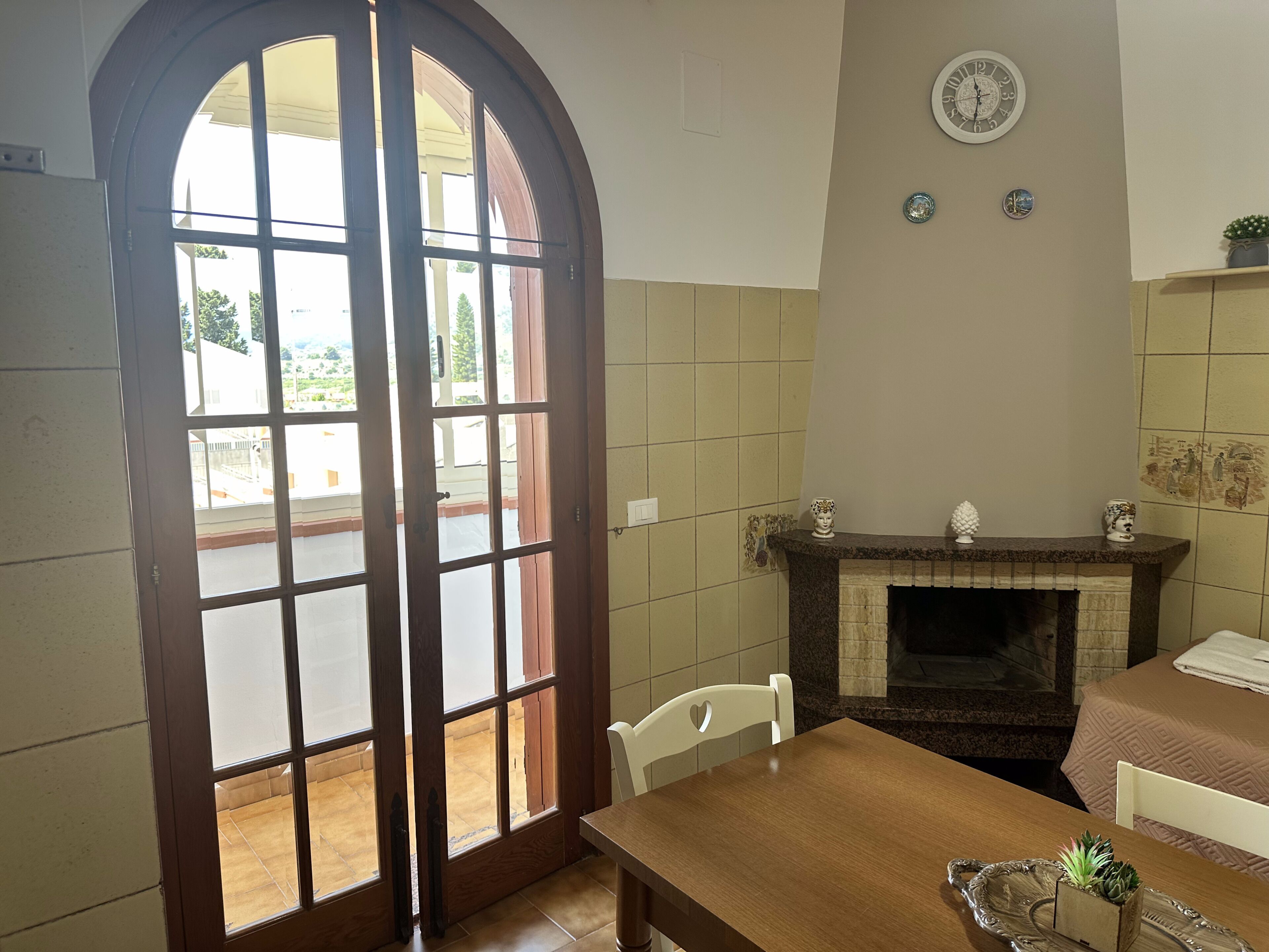 A dining area with a table and chairs, a fireplace, and a view through a large arched window.