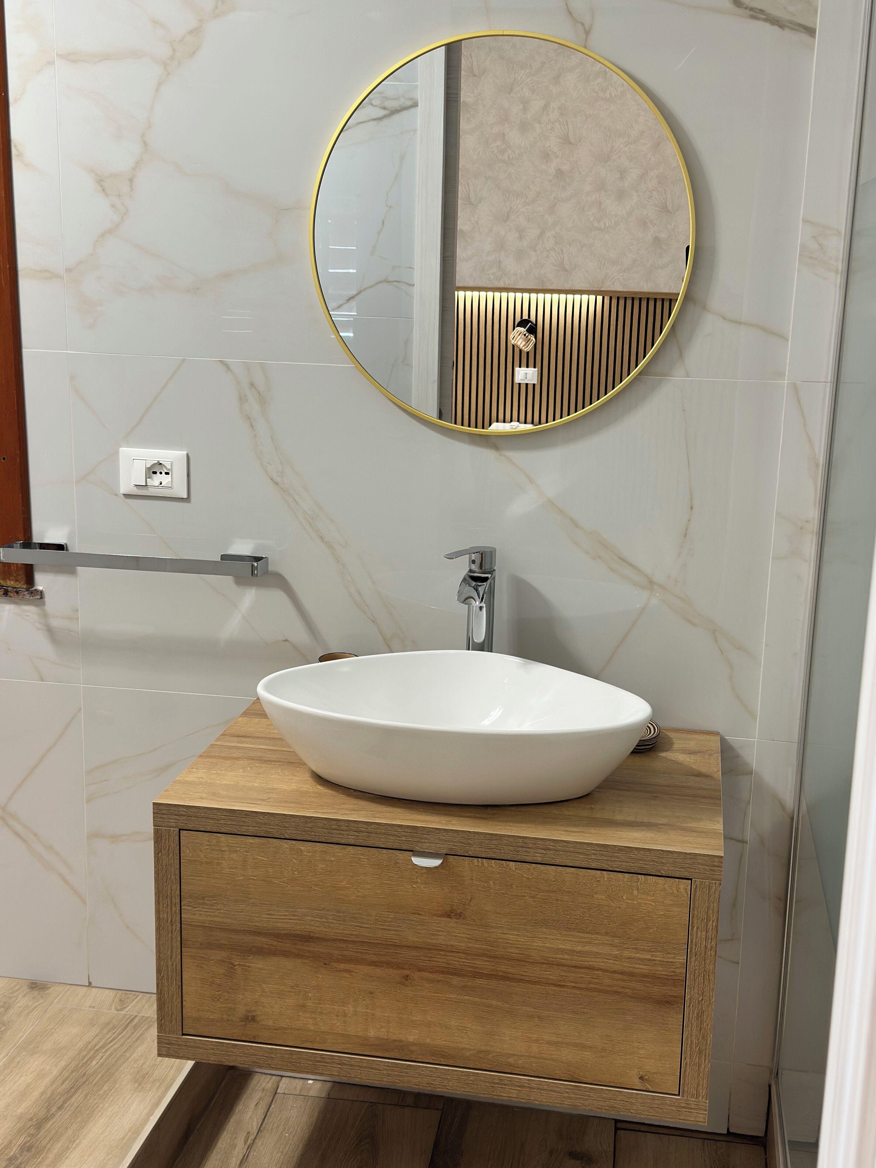 A bathroom with a wooden vanity, a white sink, a round mirror, and a towel rack.
