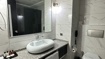 A modern bathroom with a large mirror, a white sink, a toilet, and a shower area.