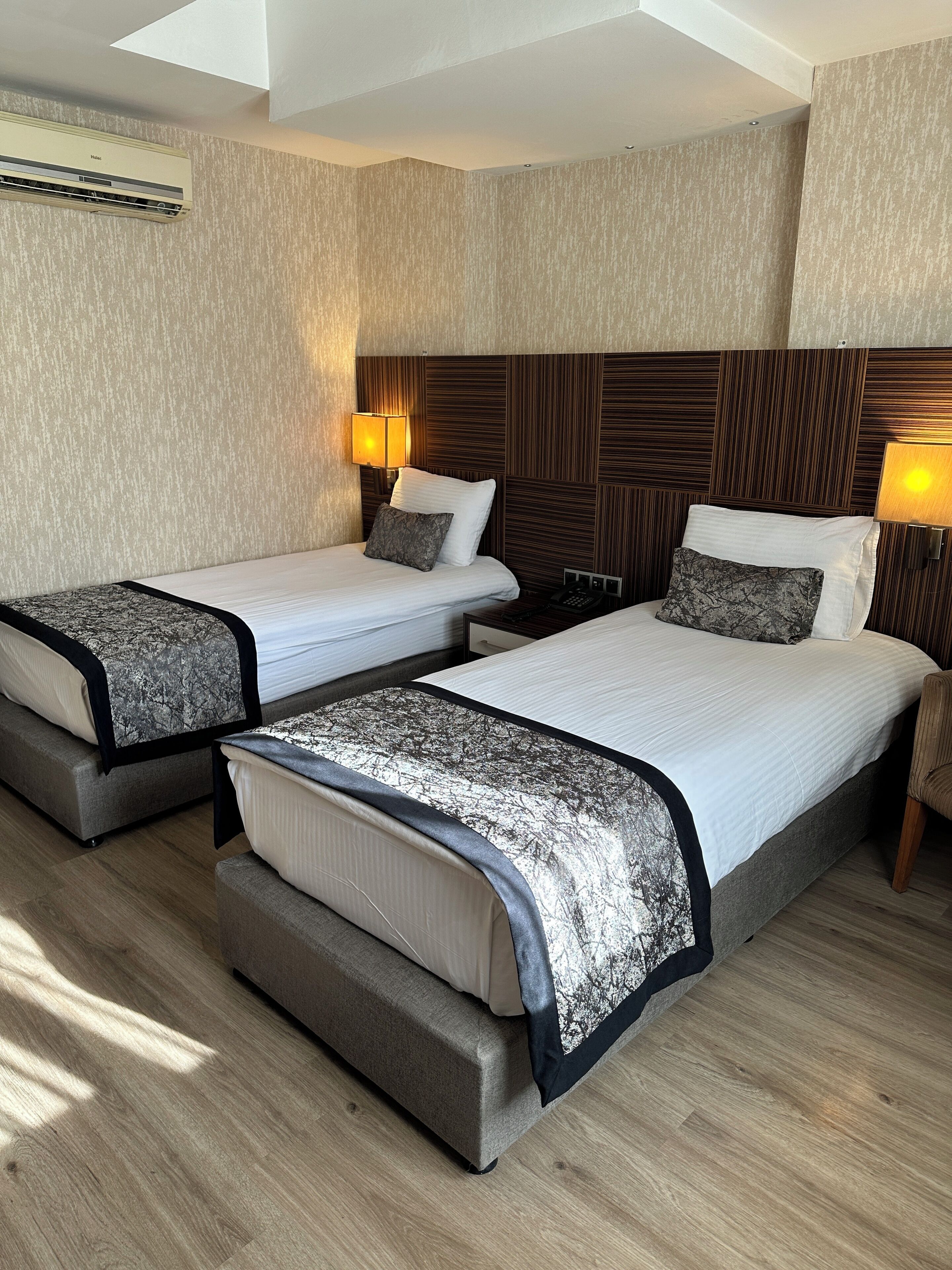 A hotel room with two beds, each with a headboard, bedside tables, lamps, and a ceiling fan.