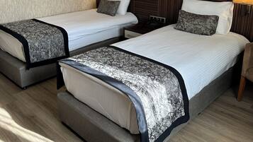 A hotel room with two beds, each with a headboard, bedside tables, lamps, and a ceiling fan.