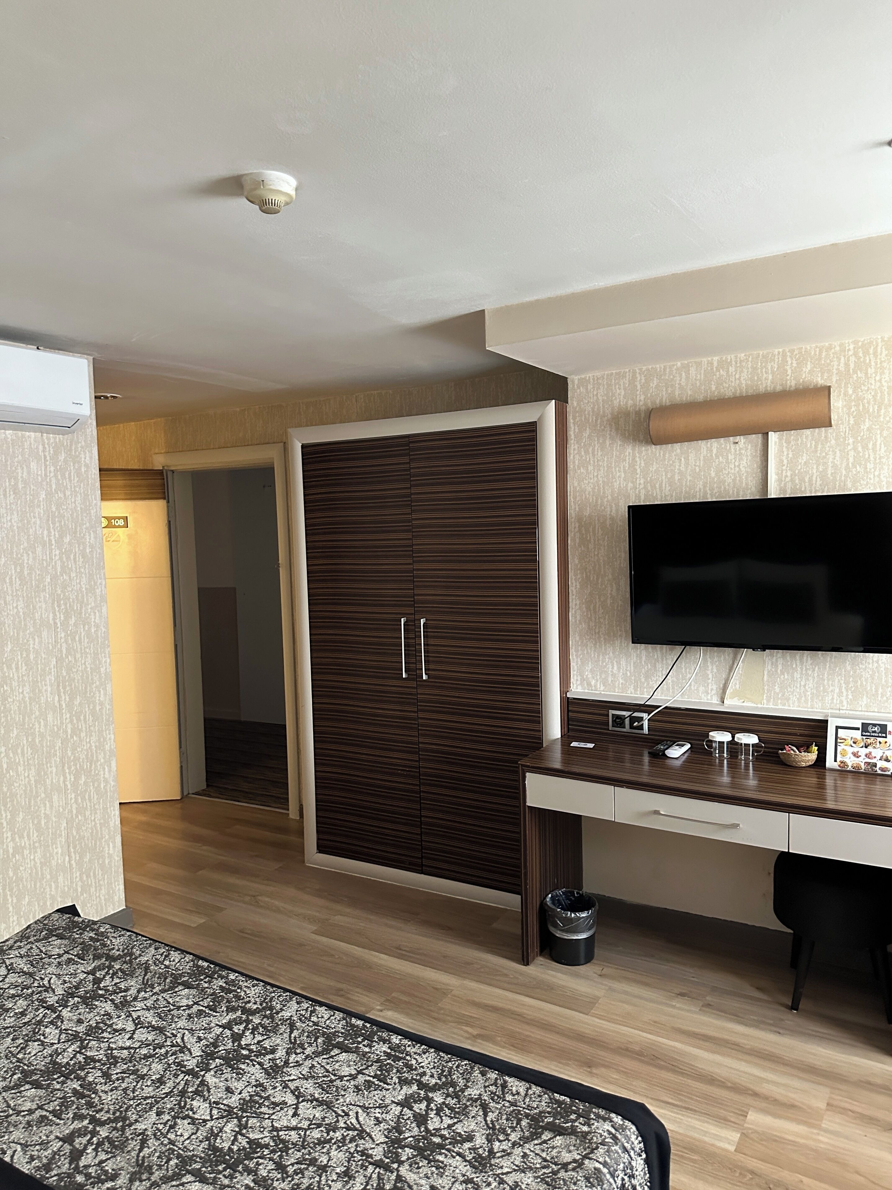 Una habitación de hotel moderna con un armario de madera, un televisor de pantalla plana, un escritorio con cafetera y una alfombra estampada.